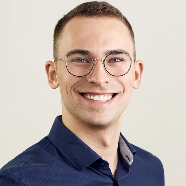 Porträt von Lasse Kisthardt, lächelnd, mit runder Brille und dunkelblauem Hemd.